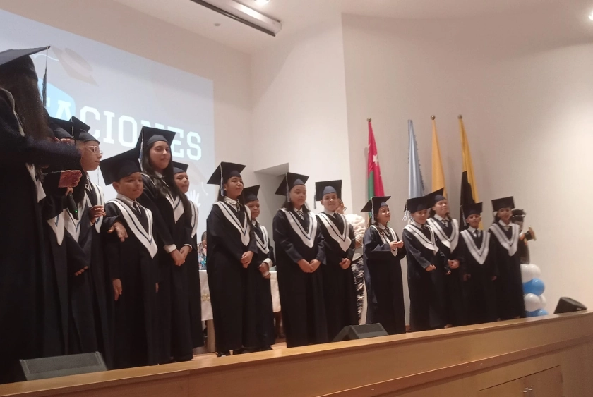 Estudiantes del Liceo Jesús de Nazareth vestidos con toga y birrete negro, alineados en un escenario durante su ceremonia de graduación.